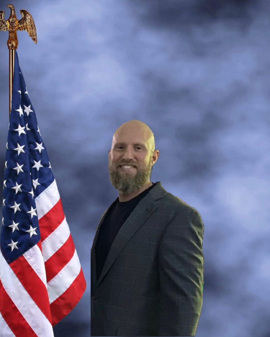 A bald man standing next to an american flag.