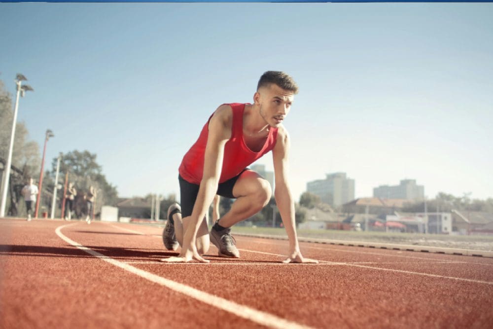 A man is crouching on the track in a red shirt