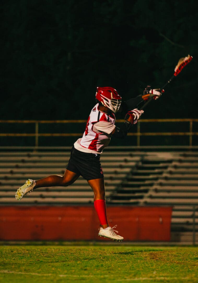 A lacrosse player is jumping in the air with his stick.